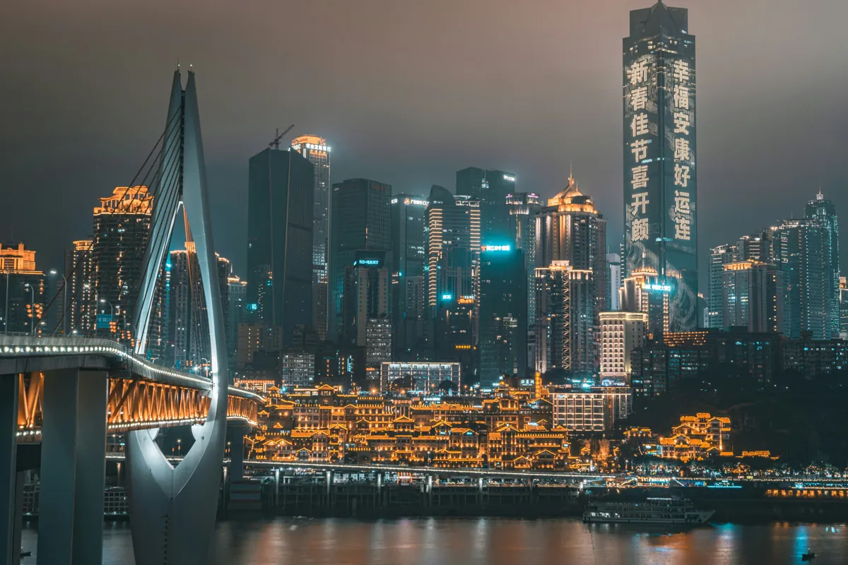 Night view of Hongya Cave (洪崖洞) and the skyscrapers of downtown Chongqing, with Qiansimen Bridge lit up over the Jialing River.